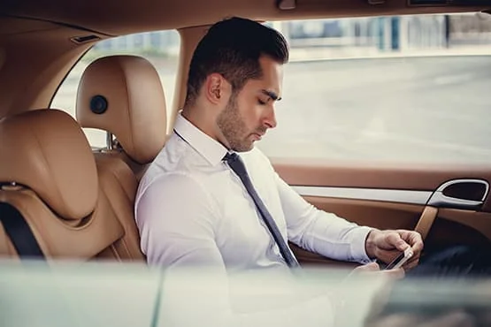 Un homme en chemise et cravate consulte son téléphone à l’arrière d’une voiture.