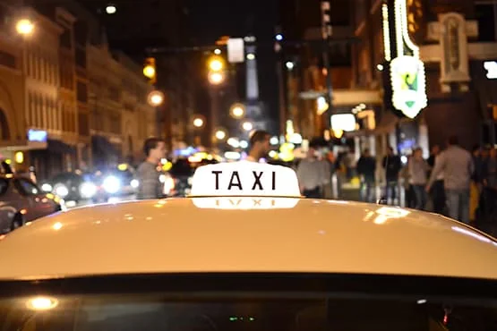 Lumignon « TAXI » sur une voiture dans une rue éclairée de nuit.