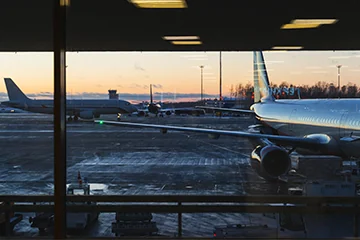 Avions stationnés sur le tarmac, vus à travers les vitres d’un terminal au crépuscule.