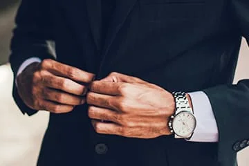 Un homme en costume ajuste le bouton de sa veste, en gros plan.