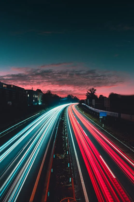 Traînées lumineuses de véhicules sur une route au crépuscule.